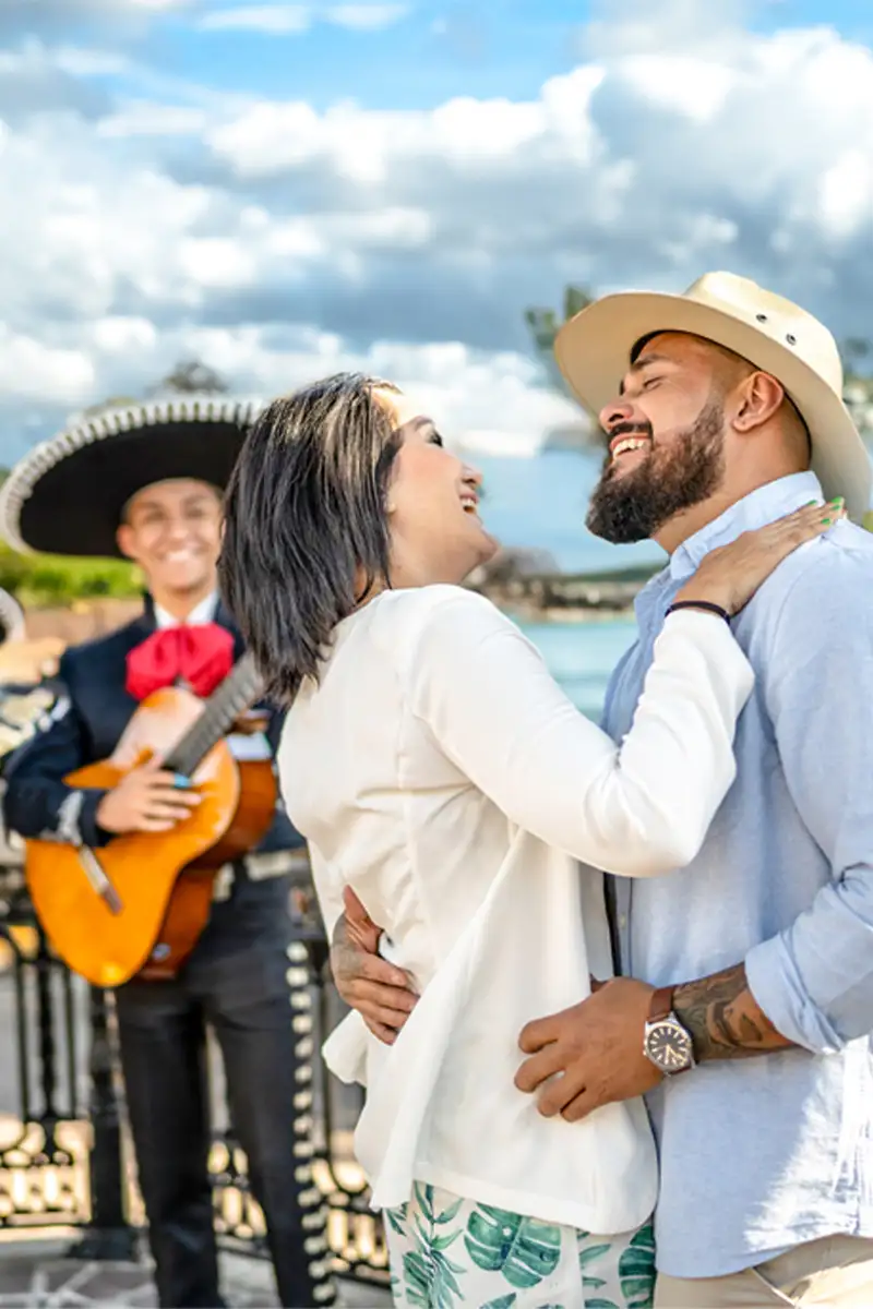 Smiling adult couple dancing joyfully in front of a group of mariachis playing in the background.