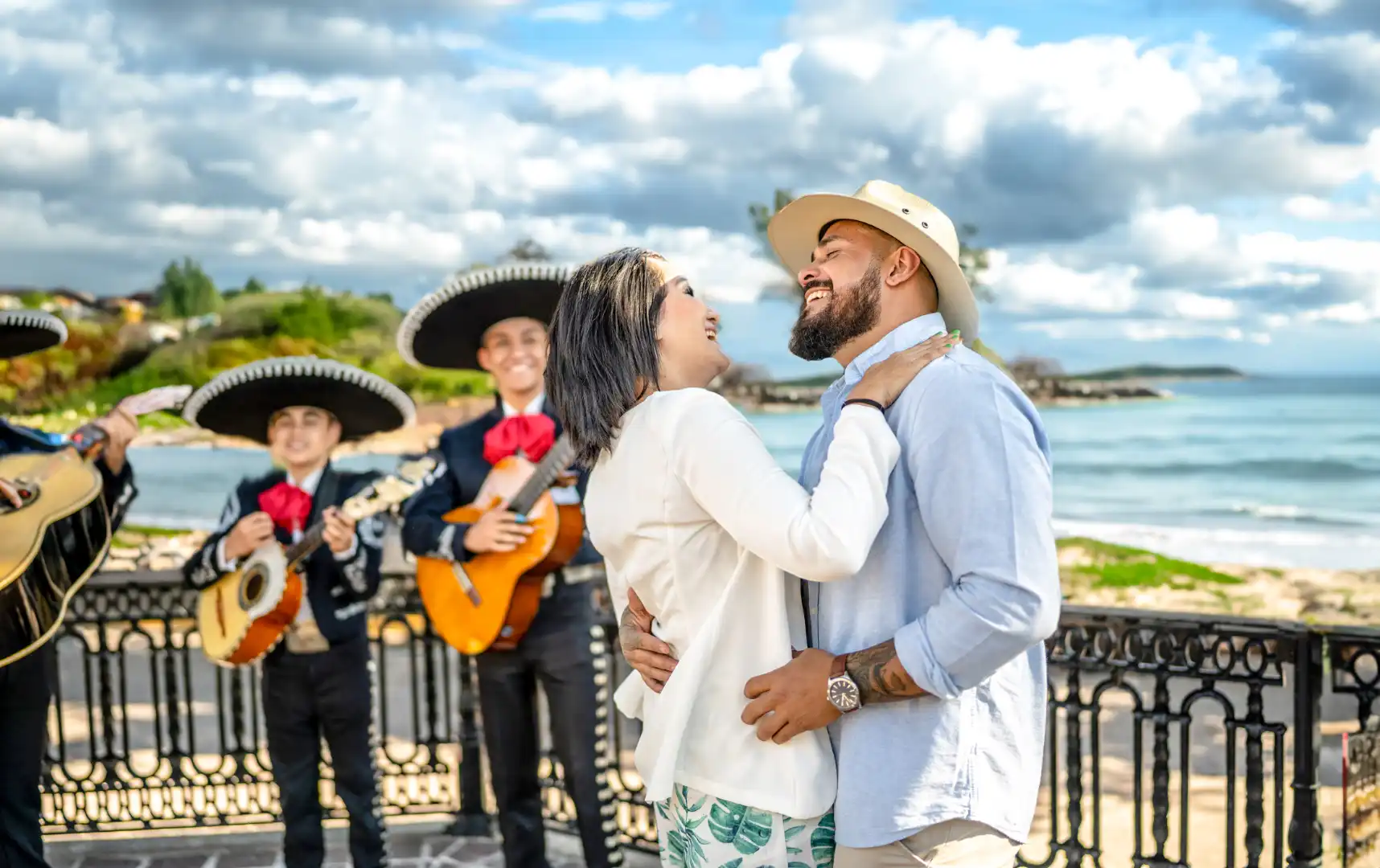 Smiling adult couple dancing joyfully in front of a group of mariachis playing in the background.